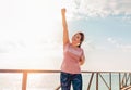 An adult woman happily raises her hand up. In the background, the sky with clouds, Sunny weather. Copy space. Concept of human Royalty Free Stock Photo