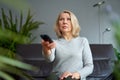 Adult woman at home sitting on the couch and watching tv, she is holding a remote control. Royalty Free Stock Photo