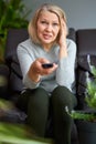 Adult woman at home sitting on the couch and watching tv, she is holding a remote control. Royalty Free Stock Photo