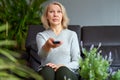 Adult woman at home sitting on the couch and watching tv, she is holding a remote control. Royalty Free Stock Photo