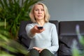 Adult woman at home sitting on the couch and watching tv, she is holding a remote control. Royalty Free Stock Photo