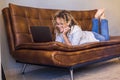 Adult woman lay down on te sofa and use laptop computer smiling and having fun alone at home - people female and internet online