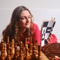 Adult woman learns chess while sitting with a book at a chessboard