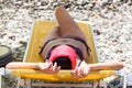 Adult woman lying in shadow of parasol on pebble beach, sunbathing alone on sea coast Royalty Free Stock Photo