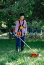 Adult woman mows the grass in the backyard using string trimmer. Garden work concept Royalty Free Stock Photo