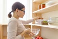 Adult woman picking food from storage cabinet in kitchen, storage with wooden shelves Royalty Free Stock Photo