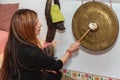 Adult woman playing gong- music therapy. Portrait of a happy woman striking a gong for meditation.