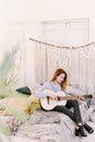 An adult woman plays the guitar sitting on the bed in a boho style room. Nice and cozy atmosphere Royalty Free Stock Photo