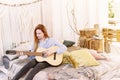 An adult woman plays the guitar sitting on the bed in a boho style room. Nice and cozy atmosphere Royalty Free Stock Photo