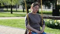 Adult woman riding swing sits with upset expression in park