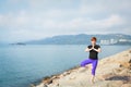 Adult woman with short red hair in sportswear doing yoga exercise outdoors with sea views