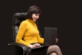 An adult woman is sitting with a smile on a leather chair working at a computer on a black Royalty Free Stock Photo