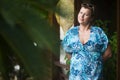 Adult woman stands in the doorway of her house in the summer and waits for guests. Blurred palm l