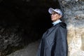 An adult woman stands at the rocky entrance to a cave, Austria, Salzburg