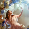 Adult woman on a swing with flowers in the rays of light. Woman in a pink dress on a background of mystical glowing clouds