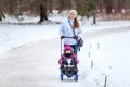 Adult woman walking with her baby on winter park, pulling sled with daughter on snow pathway, copyspace Royalty Free Stock Photo