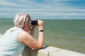 An adult woman watches the ocean through binoculars on a summer sunny day