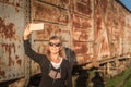 Adult woman wearing sunglasses taking a selfie with her smartphone of abandoned train cars Royalty Free Stock Photo