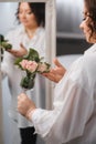 An adult woman in a white shirt is standing with a glass with roses sprinkled on it. A girl in the interior with a glass