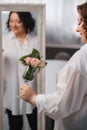 An adult woman in a white shirt is standing with a glass with roses sprinkled on it. A girl in the interior with a glass