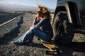 Adult woman witting on a longboard outside the car with long road in background - concept of young alternative lifestyle fredom