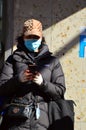 An adult woman works on her phone while wearing a face mask