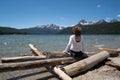 Adult woman 30-35 years sits on a pile of logs on the shoreline of Redfish Lake in Stanley Idaho in the Sawtooth Mountains in Royalty Free Stock Photo