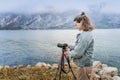 Adult young woman traveler professional photographer taking a picture of the landscape while standing with a camera on a tripod on Royalty Free Stock Photo