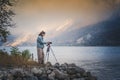 Adult young woman traveler professional photographer taking a picture of the landscape while standing with a camera on a tripod on Royalty Free Stock Photo