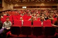 Adults and children sit on red chairs