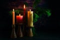 Advent arrangement with four candles in red and yellow on wooden holders and pine branches against a very dark background from