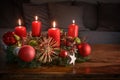 Advent wreath with four burning red candles and Christmas decoration on a wooden table in front of the couch, festive home decor Royalty Free Stock Photo