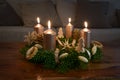 Advent wreath with four golden lit candles and natural winter decoration on a wooden coffee table at the fourth Sunday before