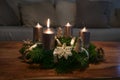Advent wreath with golden candles and natural Christmas decoration on a wooden coffee table, one flame burns for the first of four