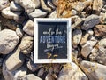 `And so the adventure begins` inspirational sign on rocky background