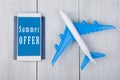 plane, passport and smartphone with text & x22;Summer Offer& x22; on white wooden table