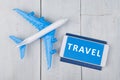 plane, passport and smartphone with word & x22;TRAVEL& x22; on white wooden table