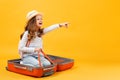 Adventure travel trip dream concept. A cheerful little girl sits inside a suitcase and shows her hand forward.