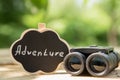 Adventure waiting for you concept small sign with Adventure inscription and binocular outdoors, green blurred background