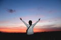 Adventure woman standing alone with arms raised against colorful sunset sky.