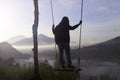 Adventure woman standing on natural wooden swing, enjoying misty mourning view in the mountain.