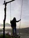 Adventure woman standing on natural wooden swing, enjoying misty mourning view in the morning. Person relax on swing.