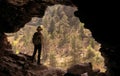 ADVENTURER WITH HAT AND BACKPACK IN A CAVE IN FRONT OF A PINE FOREST Royalty Free Stock Photo