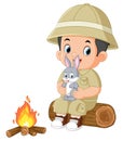 an adventurous boy sits on a fallen tree and holds a rabbit while lighting a bonfire