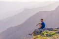 Adventurous man sitting on top of a mountain and enjoying the beautiful view, while looking downhill at the blue river and amazing Royalty Free Stock Photo