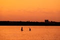 Adventurous people on a stand up paddle board is paddling during a bright and vibrant sunrise