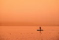 Adventurous people on a stand up paddle board is paddling during a bright and vibrant sunrise