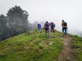 Adventurous trekking group with backpacks and walking sticks conquering a misty, steep mountain at Nag Tibba, Uttarakhand, India.