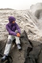 Adventurous woman is sitting next to the great Dettifoss waterfall in Iceland watching the water