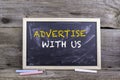 Advertise With Us. Chalk board on a wooden table Royalty Free Stock Photo